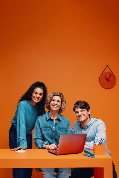 Diverse team of adults posing and smiling with a laptop in a vibrant, dynamic, and colorful office setting