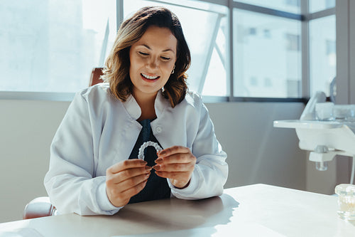 Dentist woman in dental office holding clear aligner at desk