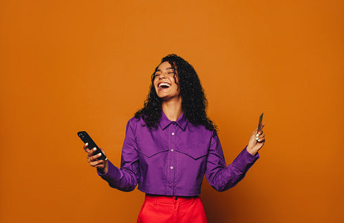 Excited woman makes online payment with credit card on orange background