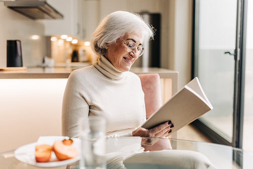 Happy senior woman reading a book at home