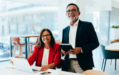 Confident professionals in office demonstrating success and teamwork with smiles and devices