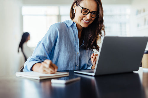 Woman making notes during an online business meeting in an office