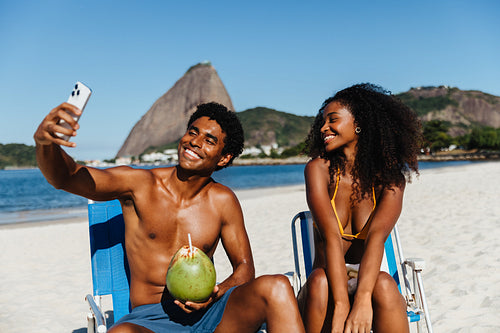 Young couple taking a selfie and relaxing with fresh coconut water at the beach