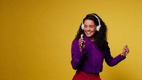Energetic young woman dancing and singing with headphones and phone