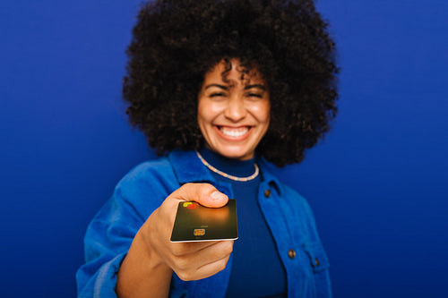 Happy woman holding out her credit card in a studio