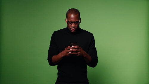 Happy African-American man laughing and texting on green screen background