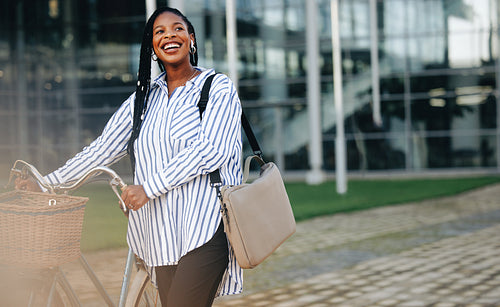Happy young businesswoman pushing her bicycle on her way to work in the city
