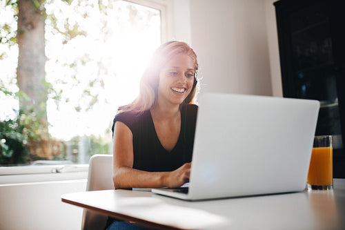 Happy female relaxing in kitchen with laptop