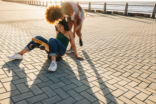 Girlfriends enjoying a skateboarding adventure on a city promenade at sunset, a carefree moment with a beautiful coastal backdrop