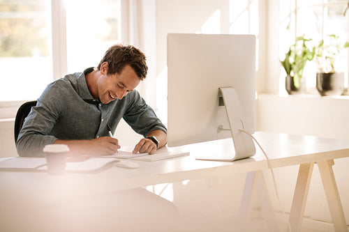 Entrepreneur making notes while working on computer at home