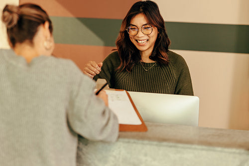 Cheerful receptionist assisting a woman with signing in to an of