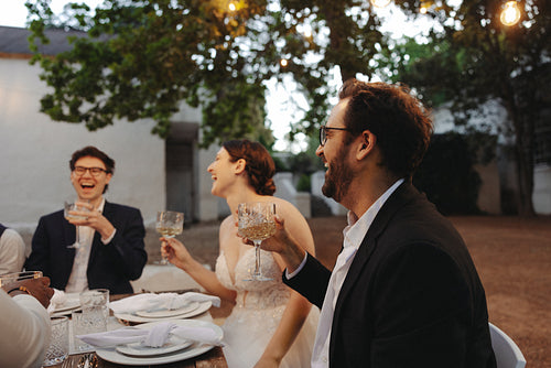 Bride and groom laughing with friends during wedding reception toast