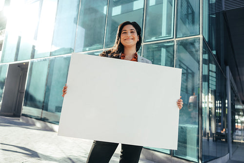 Happy businesswoman holding a white placard outside her workplace