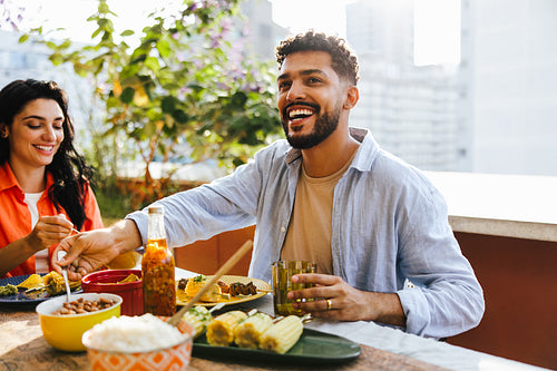Latino couple enjoying a meal at an outdoor table on a sunny day