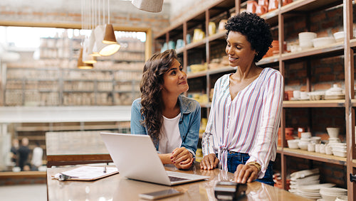 Two young ceramists smiling at each other in their shop