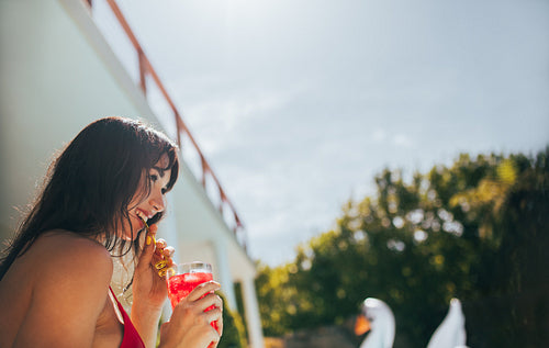 Smiling woman having a tropical drink at poolside