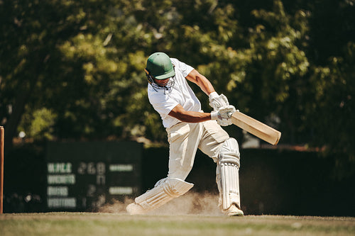Cricket player swings bat during match on a sunny day