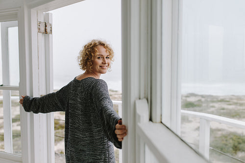 Side view of a woman standing at the door looking at the beach