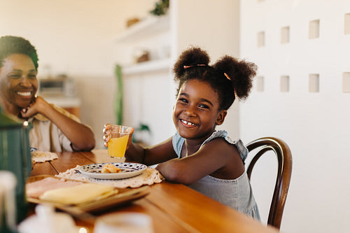 Black Brazilian girl smiling at the camera, enjoying cheese bread rolls with her mom at breakfast