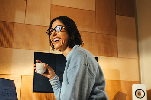 Woman smiles with coffee at her office desk while working on a laptop