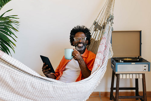 Hammock relaxation: Mature man enjoying Brazilian coffee and social media on a tablet