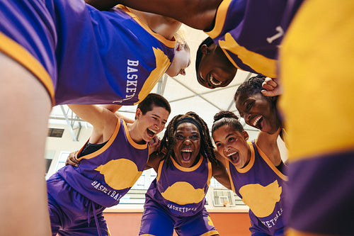 Diverse basketball team celebrating and uniting in a huddle on the court