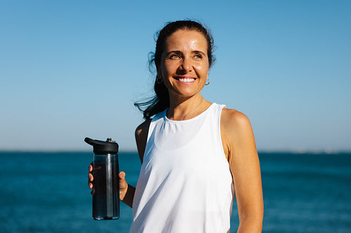Smiling woman enjoys outdoors with a water bottle by the sea