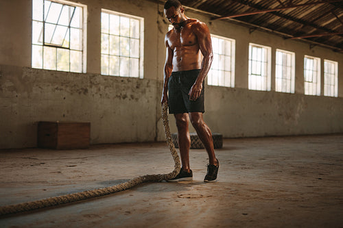 Muscular man in fitness studio with battle rope