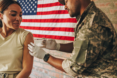 Young military physician vaccinating a female soldier in the arm