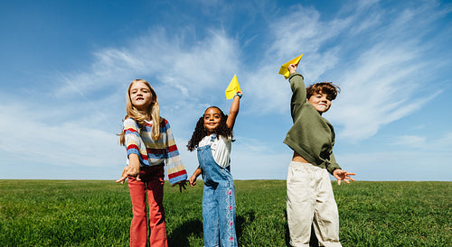 Three children playing with paper airplanes outdoors