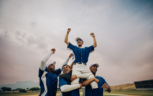 Baseball team celebrates as team members triumphantly lift a player into the air