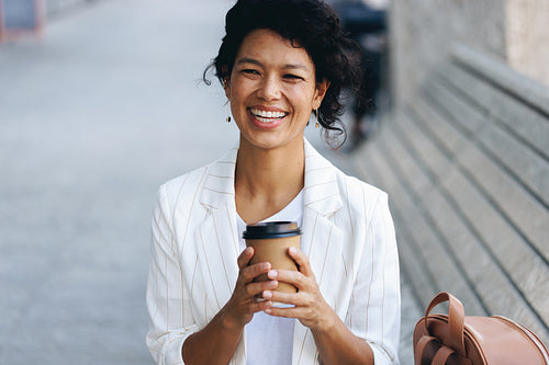 Smiling businesswoman sitting on a bench holding a coffee cup on a city street
