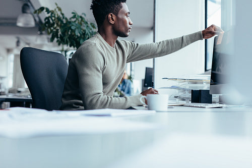 African man putting post-it note on computer monitor