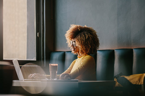 Smiling afro american woman sitting at a cafe working on laptop