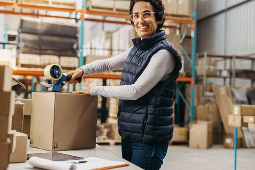 Happy warehouse worker taping a cardboard box with scotch tape