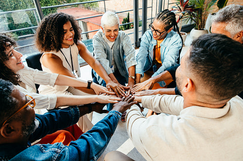 Diverse group of people coming together, placing hands in unity during a team building session in a modern office setting.