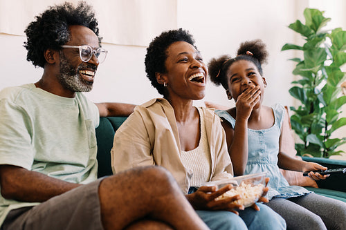 Family fun time: Parents and their child laughing and enjoying a movie together at home