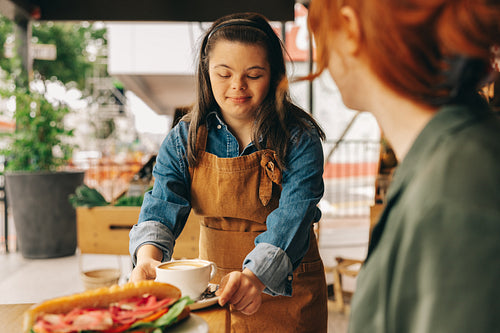 Waitron with Down syndrome serving a customer food in a cafe