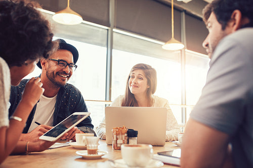 Happy young friends sitting and talking at a cafe 