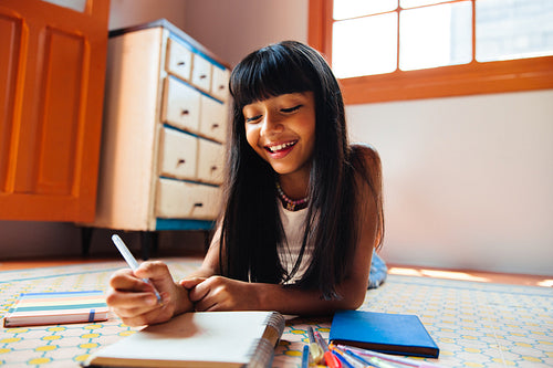 Young Latin American girl writing in a notebook while smiling and enjoying creative time