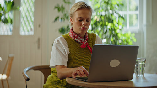 Woman works on a laptop at a cafe table in a bright indoor workspace
