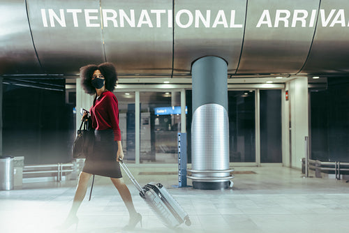 Businesswoman with face mask walking through airport terminal