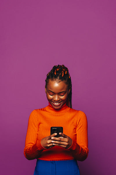 Happy young woman browsing social media on phone with colourful braids on purple background