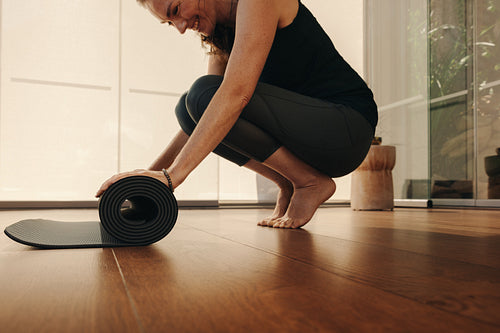 Smiling senior woman folding up a yoga mat at home