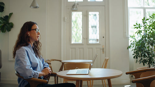 Woman speaks on a video call with laptop in a bright cafe workspace