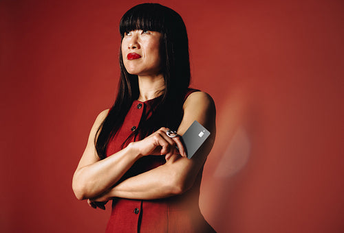 In a red studio portrait - woman holds a banking card for personal finance