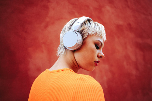Woman wears headphones for music streaming outdoors against a red wall