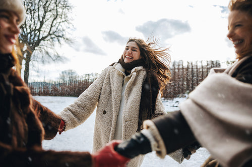 Women laugh and hold hands in snow during winter
