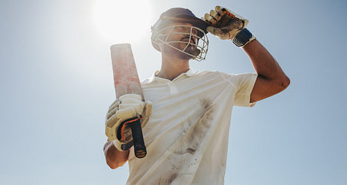 Male cricket player holding a cricket bat under a sunny sky