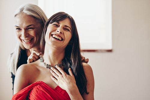 Mother standing behind her daughter holding a necklace to her neck